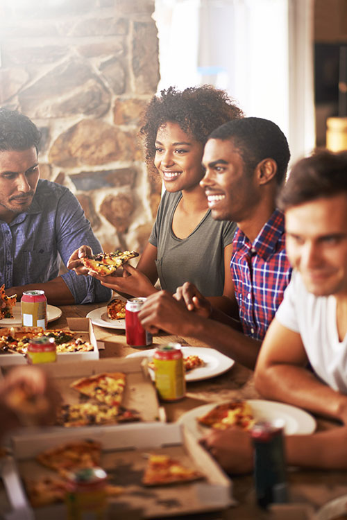 Friends-sitting-around-a-table-sharing-pizza-at-restaurant Friends sitting around a table sharing pizza at a restaurant