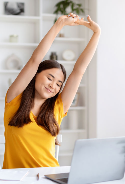 Woman-in-yellow-shirt Woman in yellow shirt stretching and smiling while sitting in front of her computer